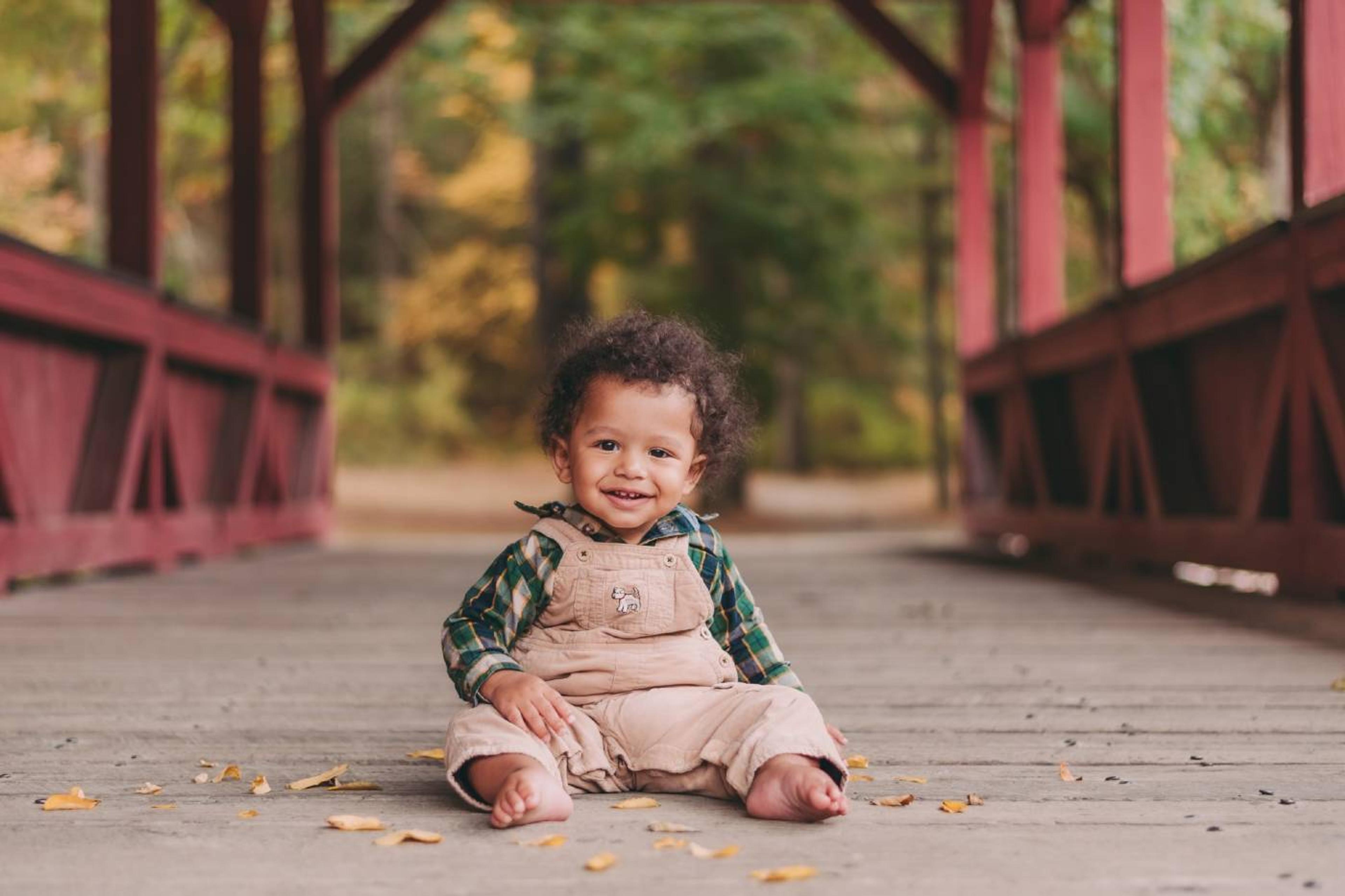 Baby boy sits on a bridge with fall foliage in the background