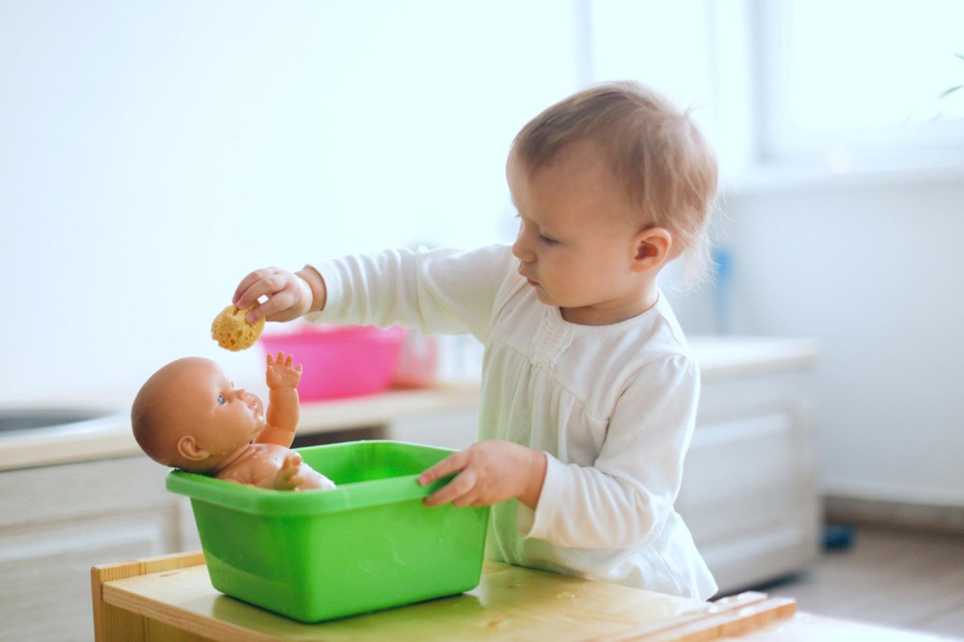 16-month-old toddler girl pretends to wash a babydoll
