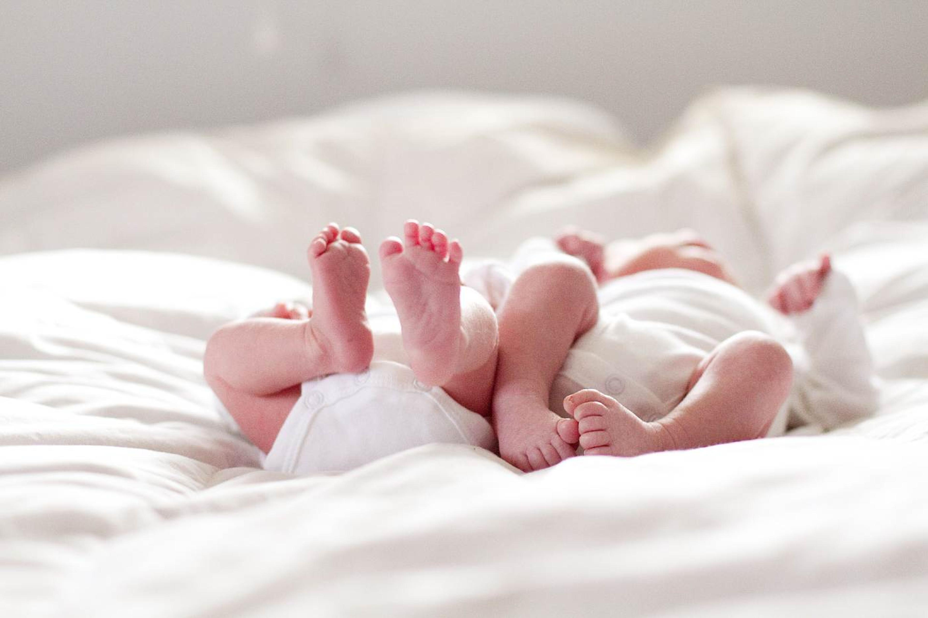 Twin babies laying on a bed.