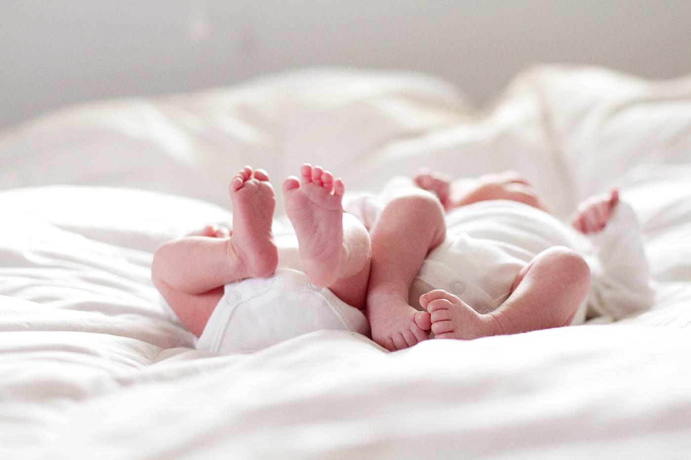 Twin babies laying on a bed.