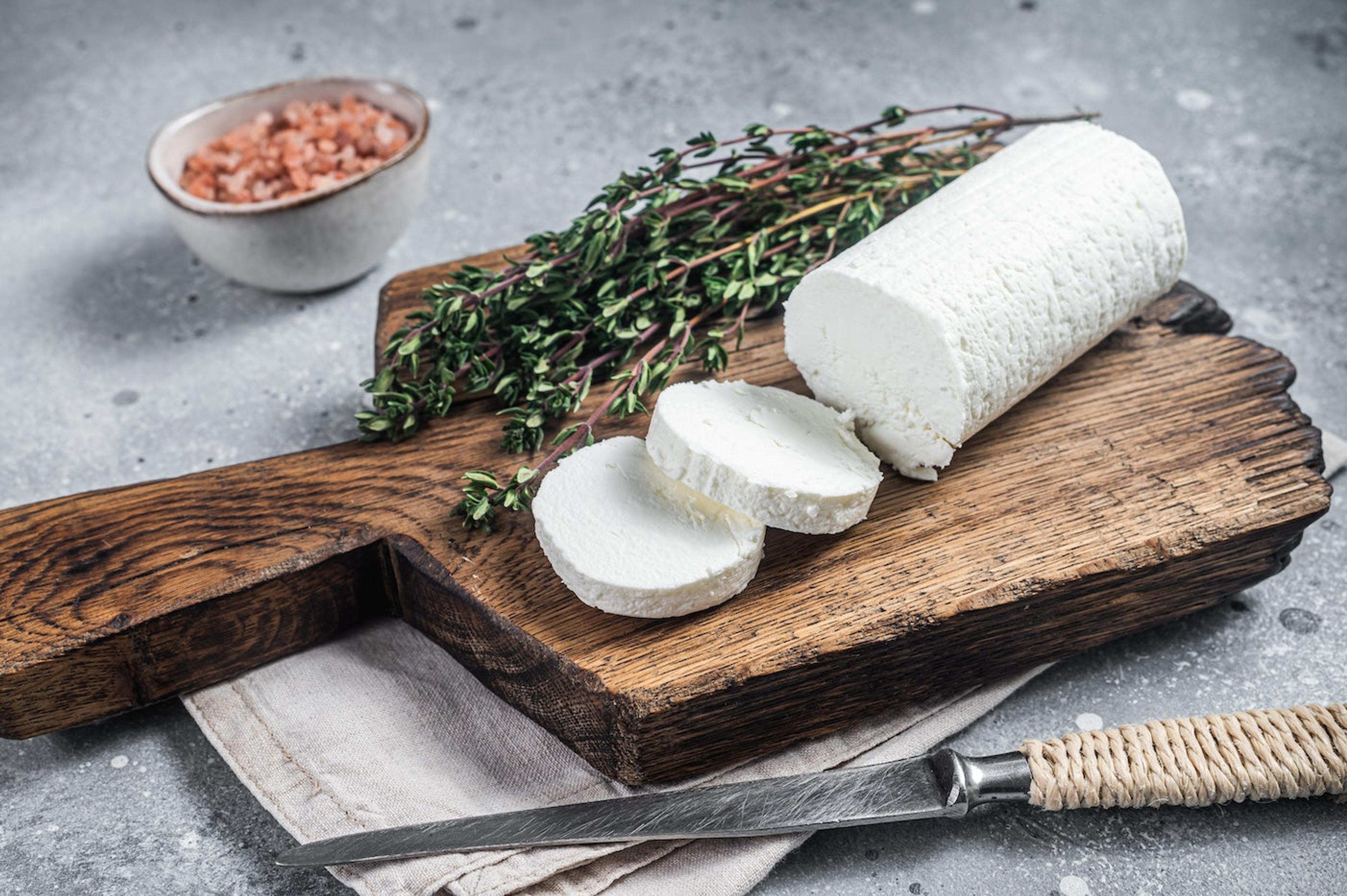 A cheese board with a log of sliced goat cheese and thyme