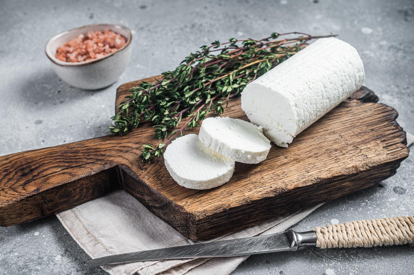 A cheese board with a log of sliced goat cheese and thyme