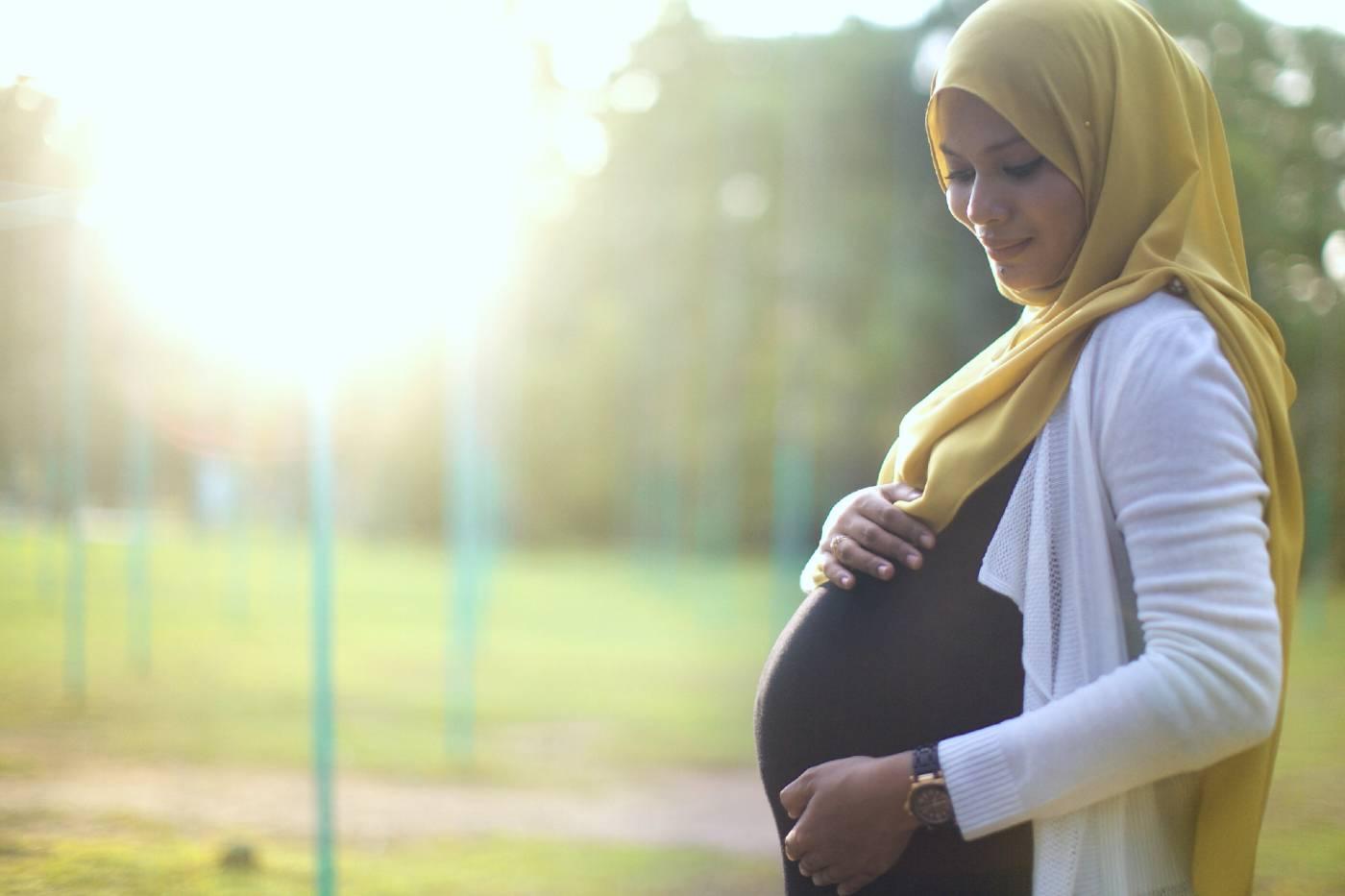 A pregnant woman stands outside and cradles her belly