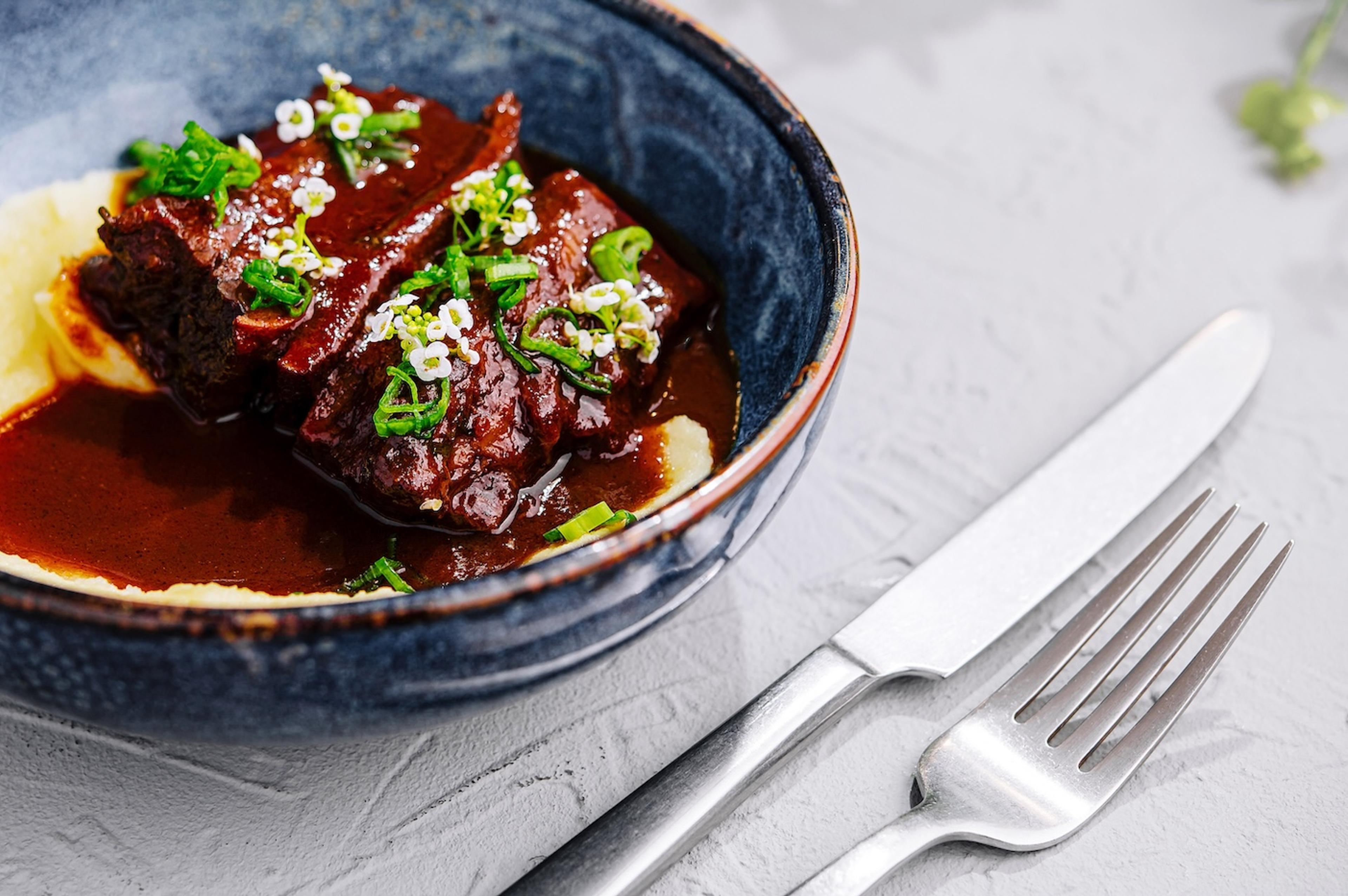 A plate of braised short ribs garnished with edible flowers