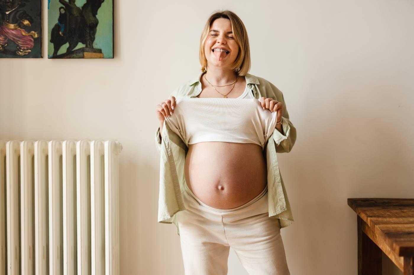 Third trimester pregnancy symptoms: Pregnant woman lifting shirt to show bump