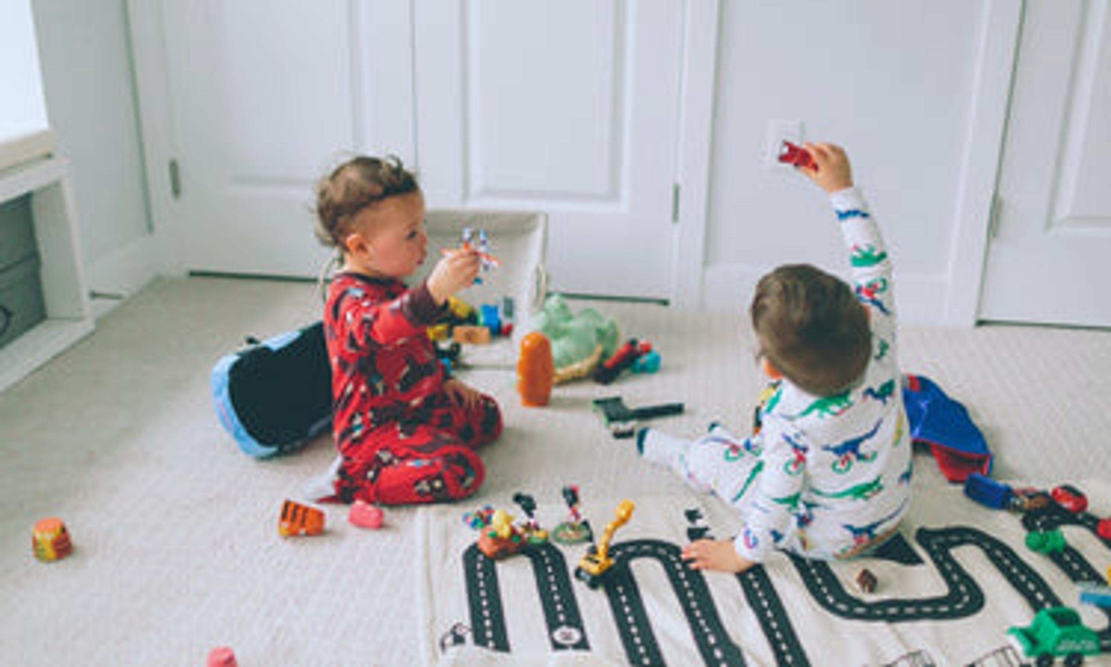Two toddler boys play on the carpet with cars and a road rug