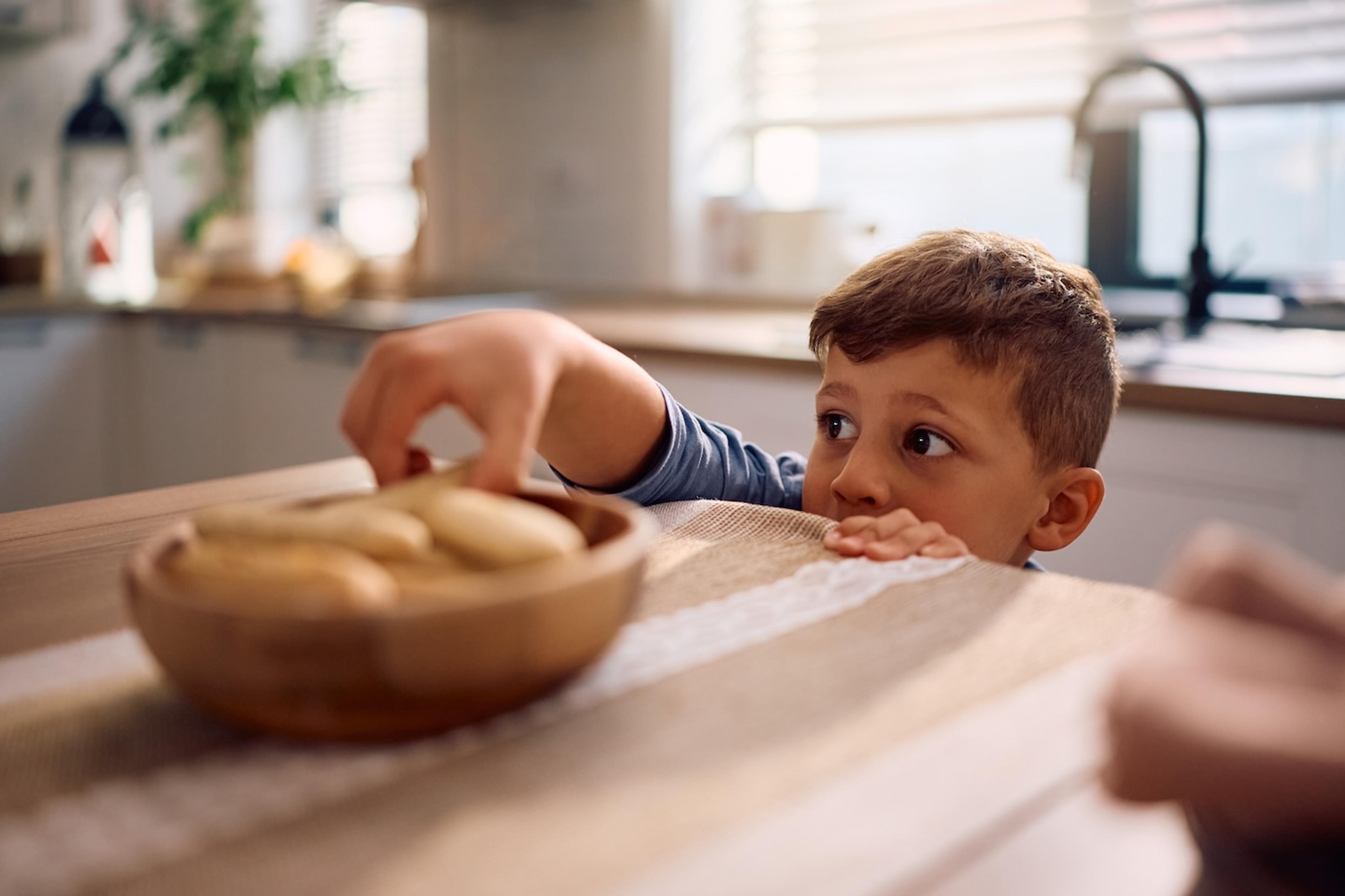 A toddler sneaks some cookies off a table