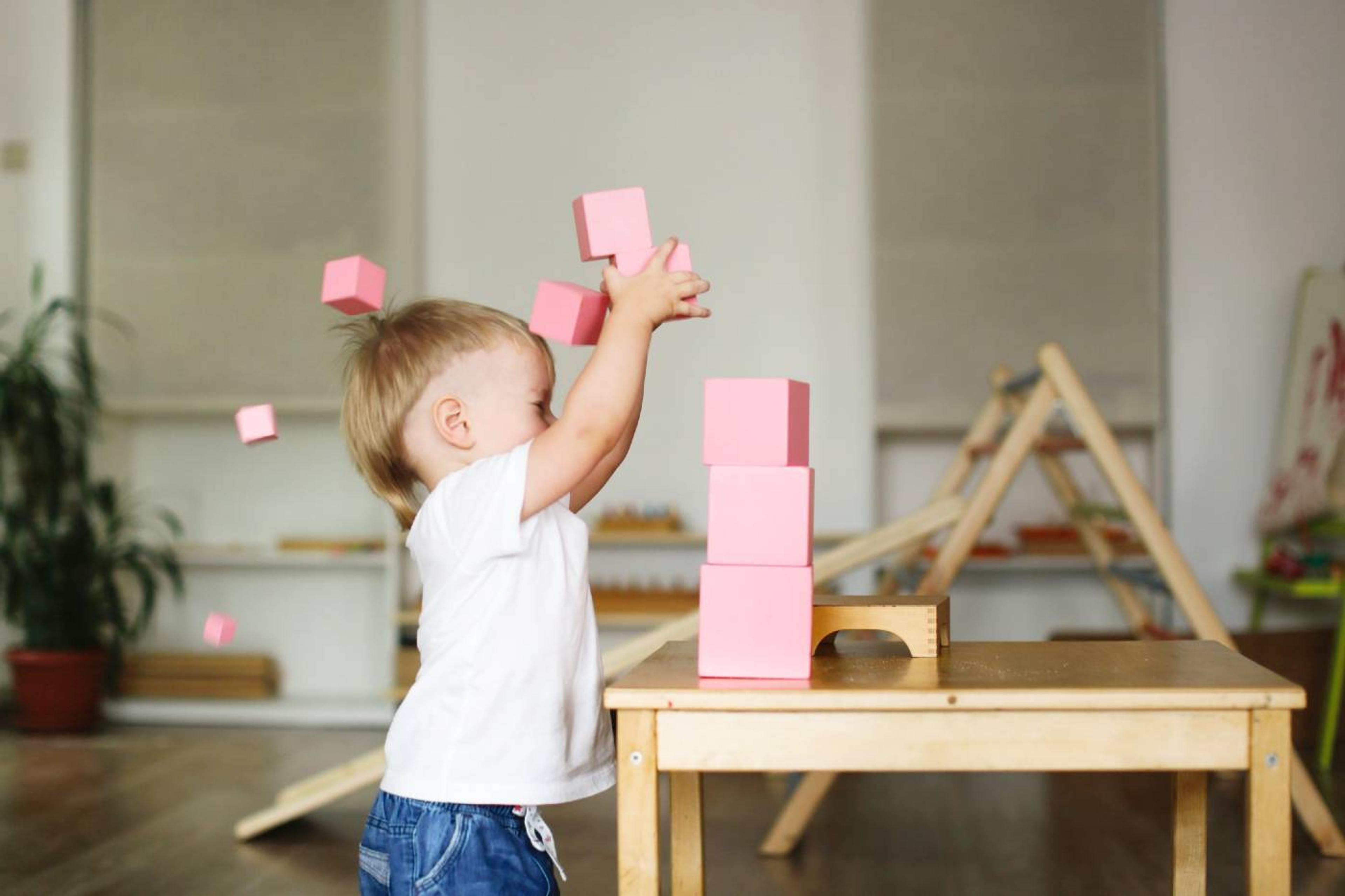 A young toddler plays with Montessori stacking blocks in his nursery