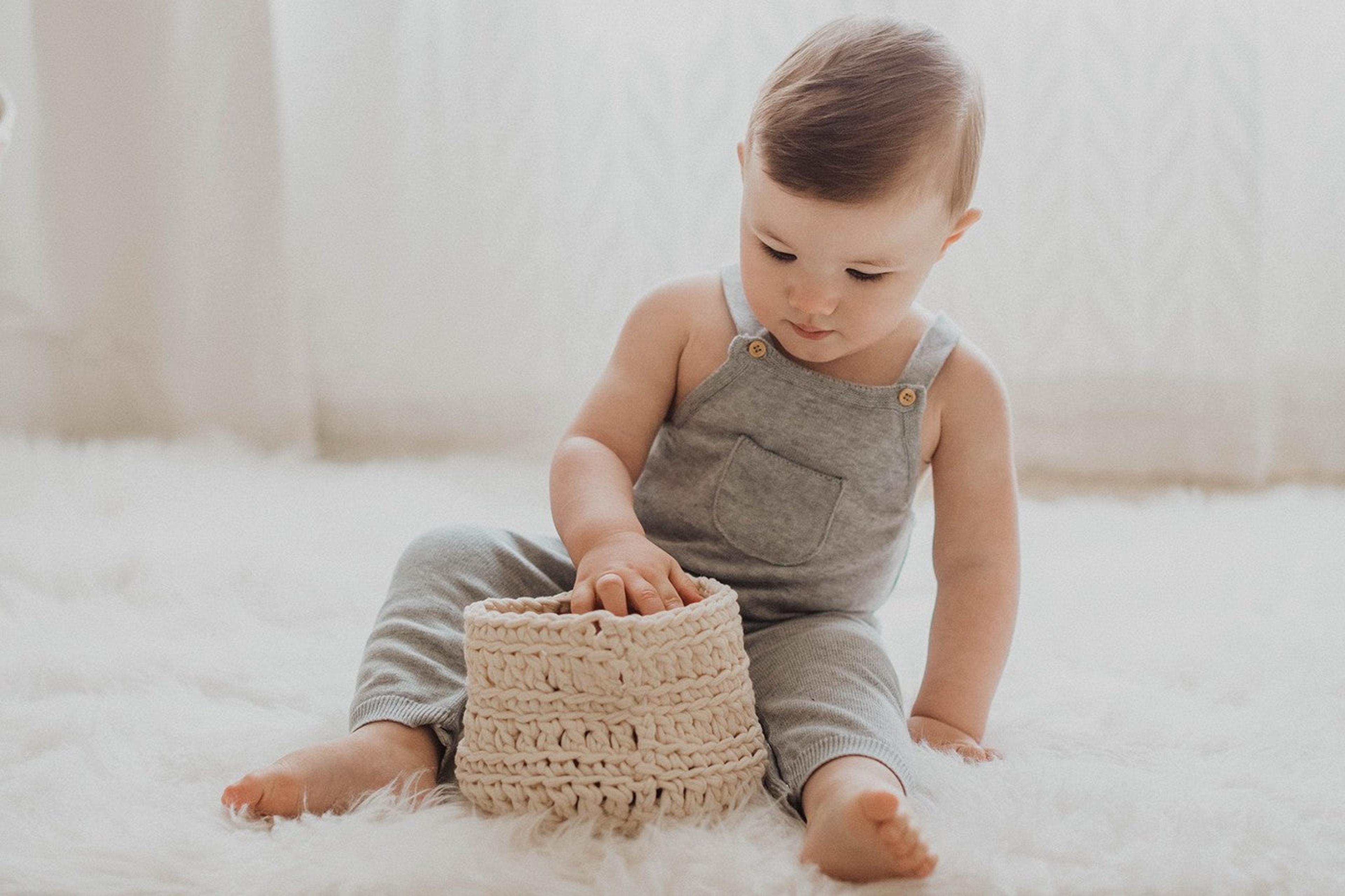 A baby explores a basket on the floor.