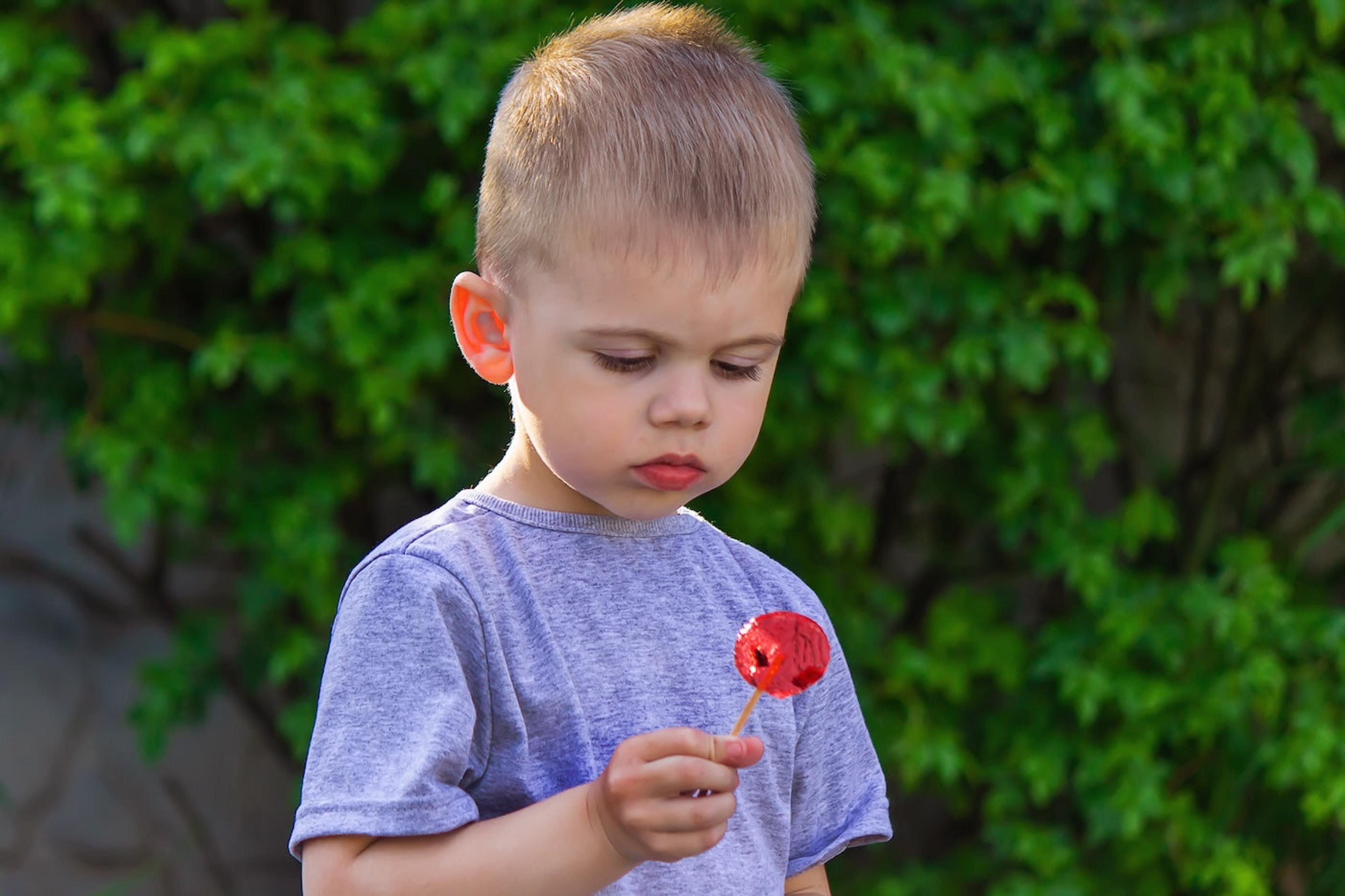 A little boy looks at a red lollipop