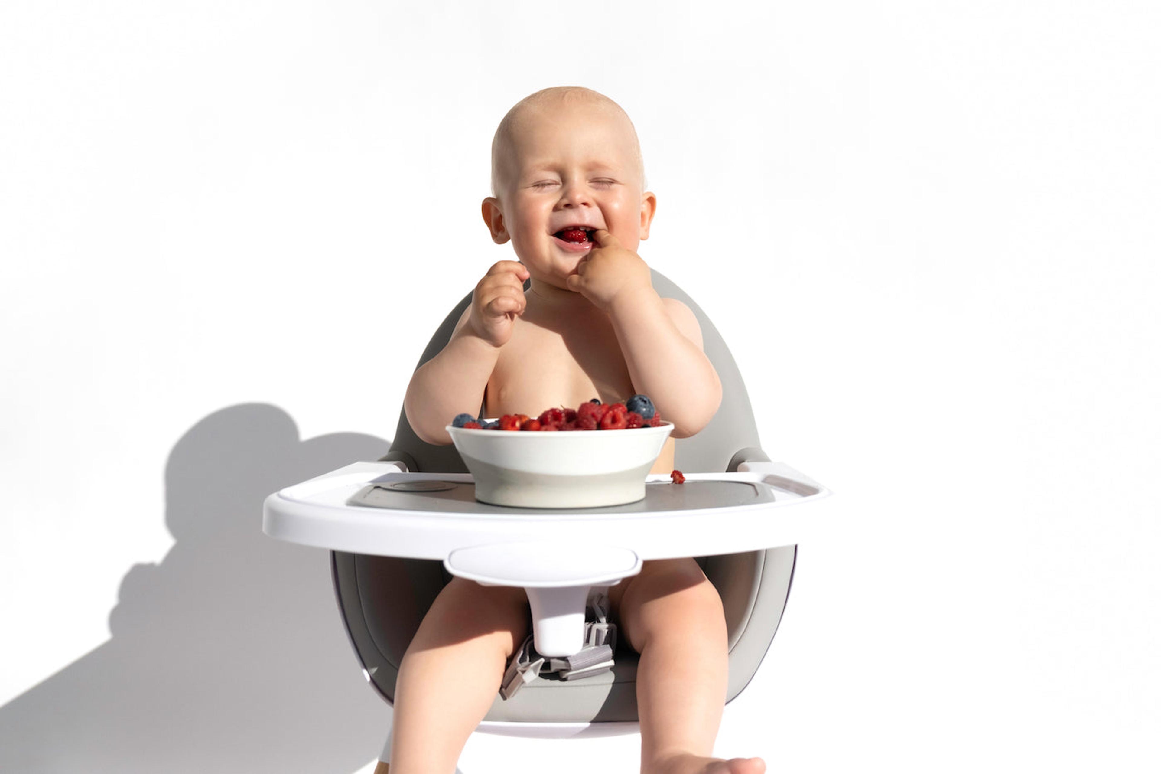 A baby is eating fiber-rich raspberries in a highchair