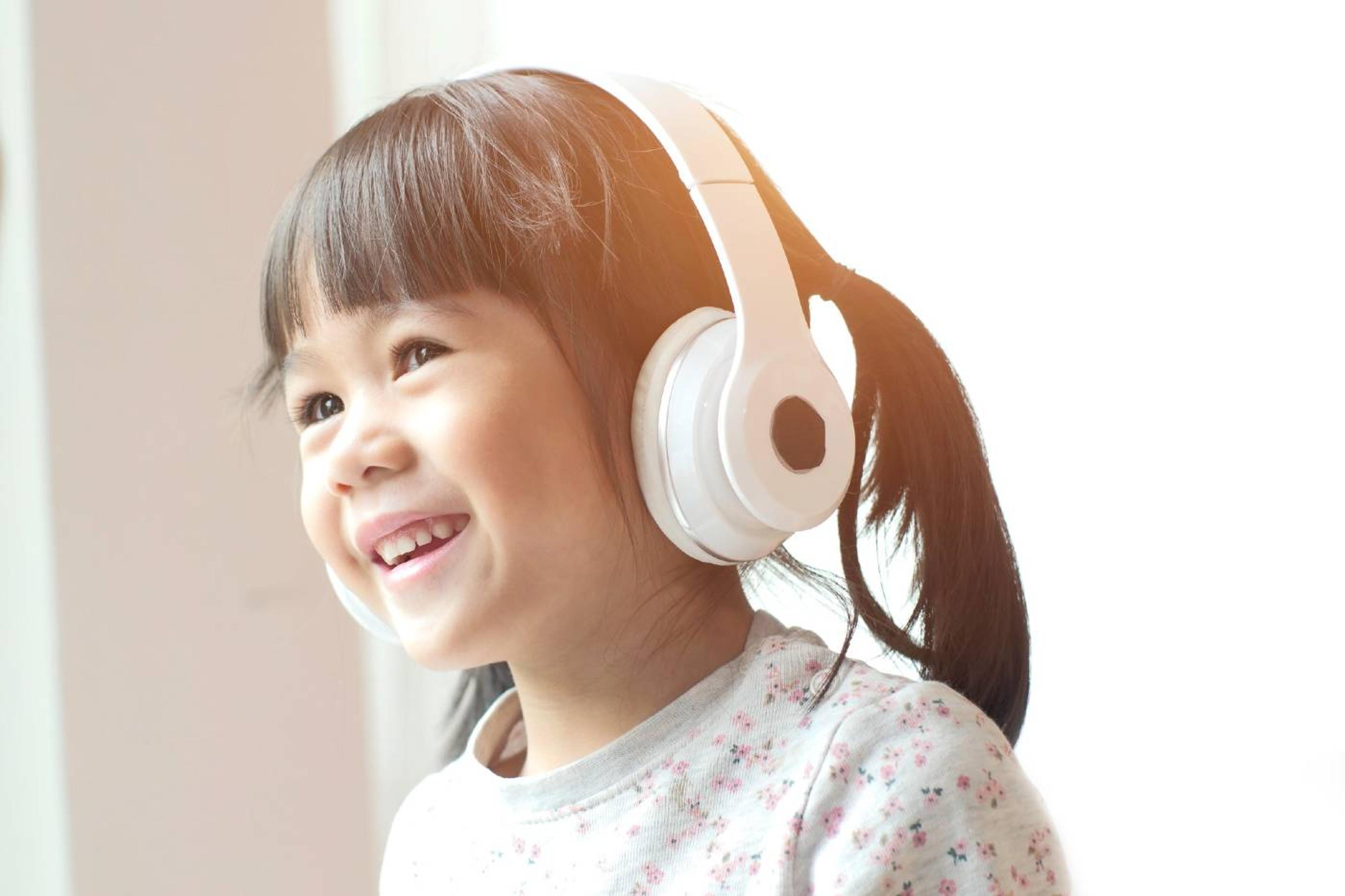 A preschool girl smiles as she listens to headphones.