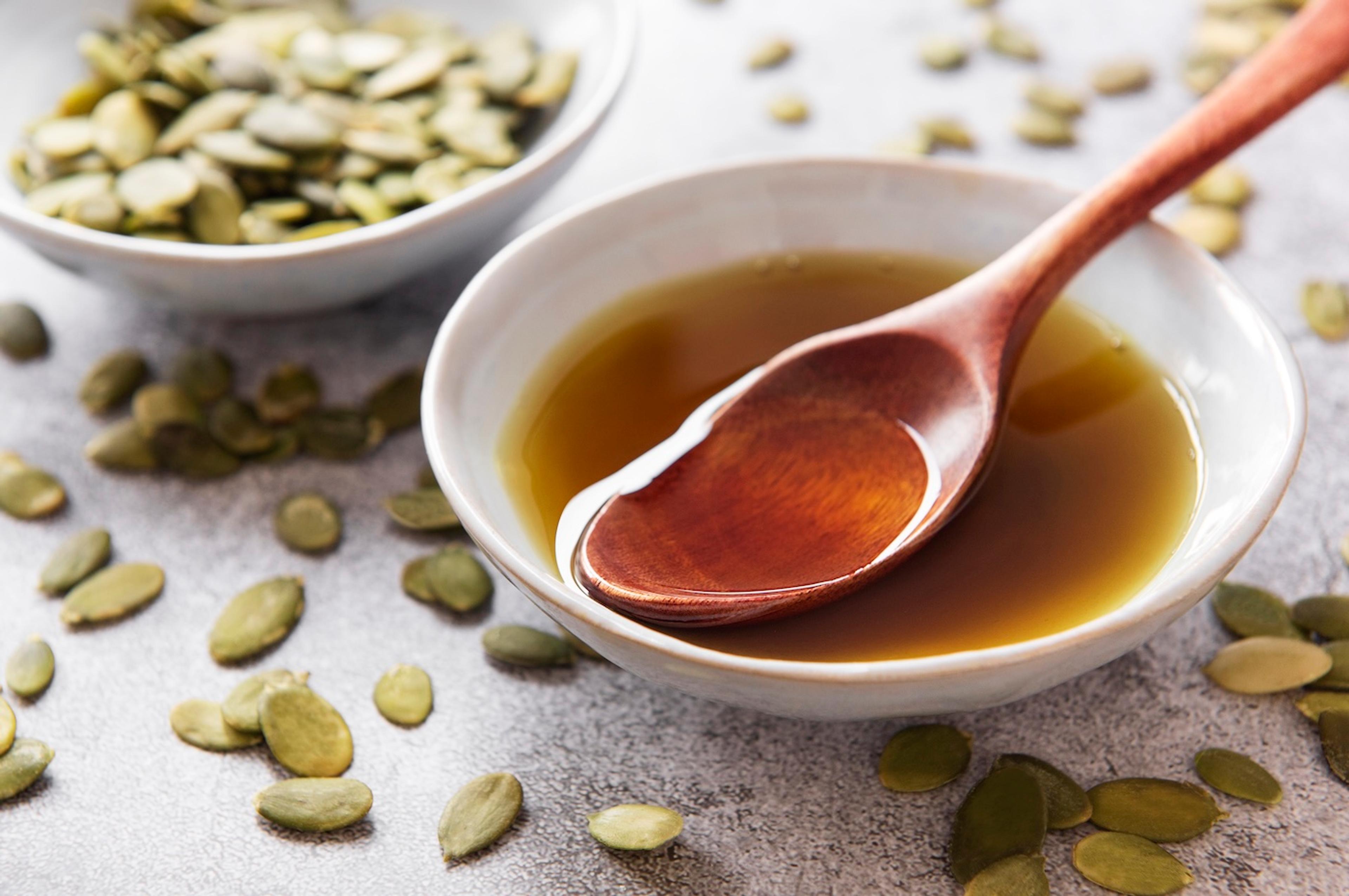 A bowl of pumpkin seed oil surrounded by pumpkin seeds