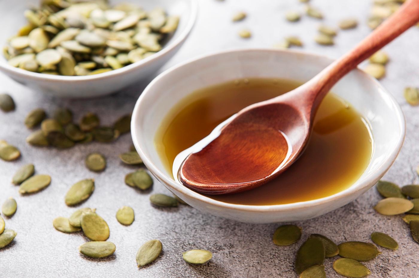 A bowl of pumpkin seed oil surrounded by pumpkin seeds
