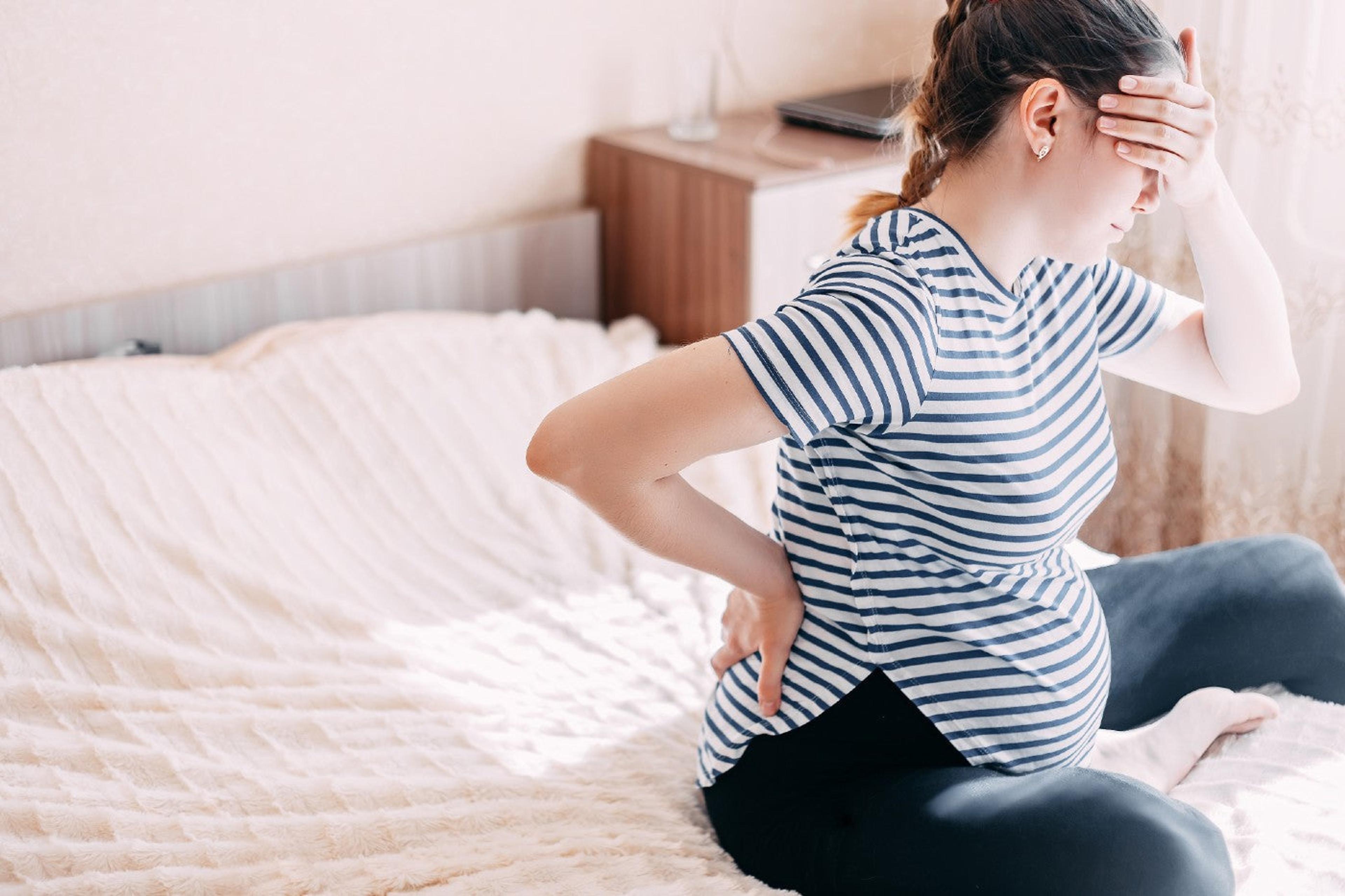 Pregnant woman sits on a bed and looks in pain