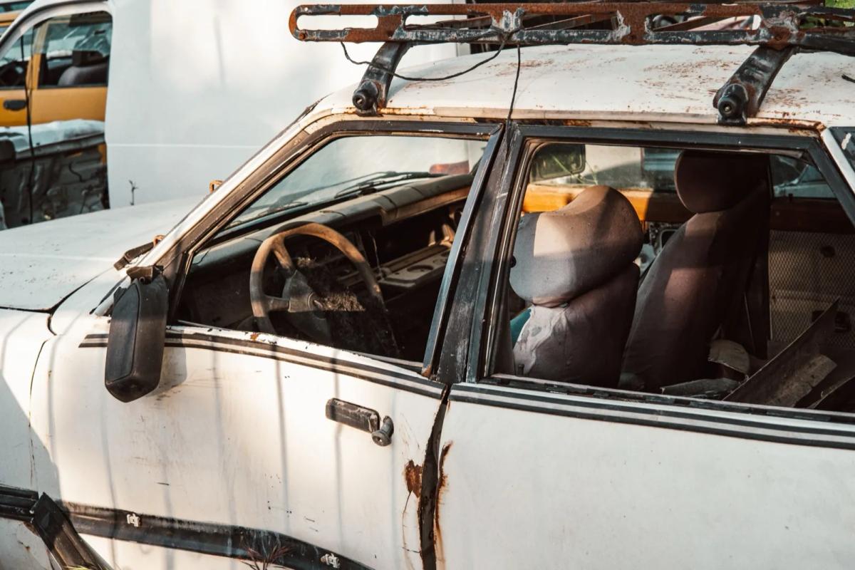 Épave de voiture abandonnée avec pneus dégonflés sur une place de parking