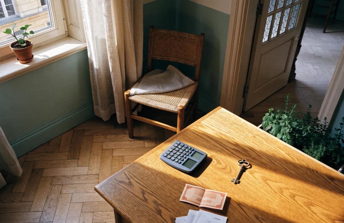 Calculatrice, billet de 50 euros, clé et documents de location posés sur un bureau