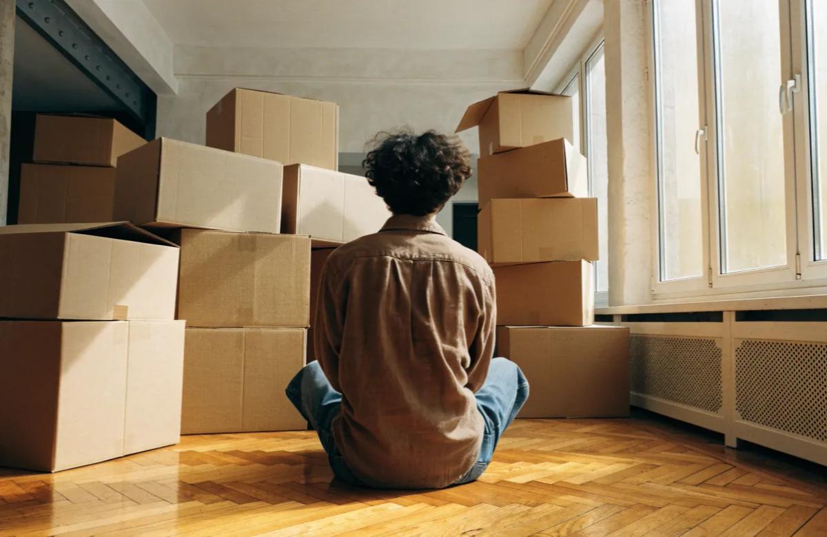 Jeune adulte entouré de cartons de déménagement dans un appartement vide