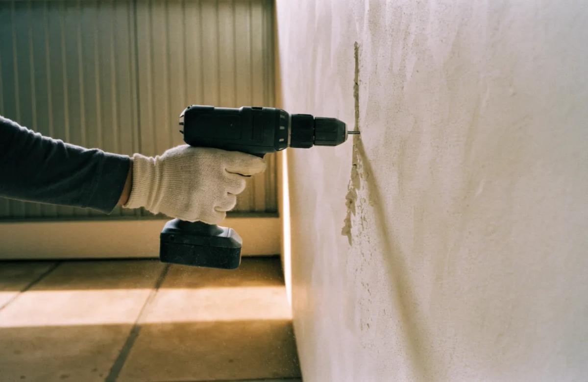 Perçage d'un mur à la perceuse, gants de protection aux mains, pour fixer le support de la caméra