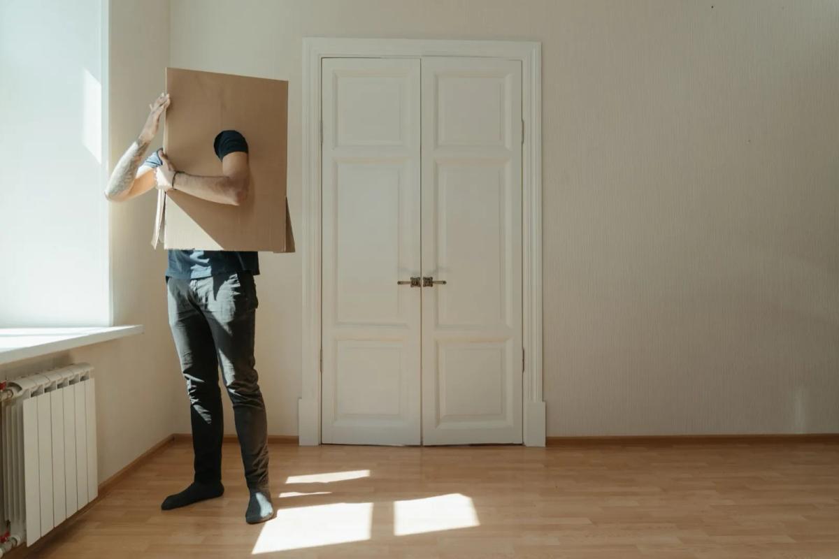 Jeune adulte entouré de cartons de déménagement dans un appartement vide