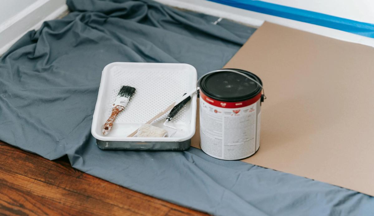 Pots de peinture et rouleaux posés sur une bâche de protection dans un appartement en cours de rénovation