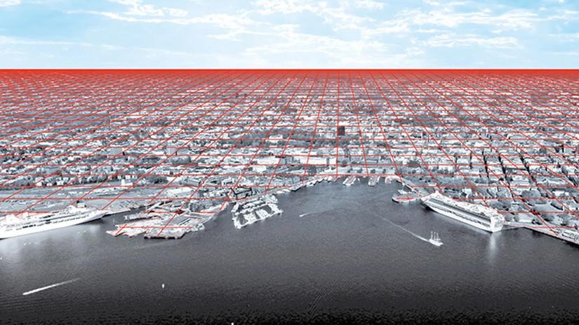 Aerial view of a cityscape overlaid with a red grid pattern extending into the horizon, depicting urban planning or network connectivity, with a waterfront and ships in the foreground.