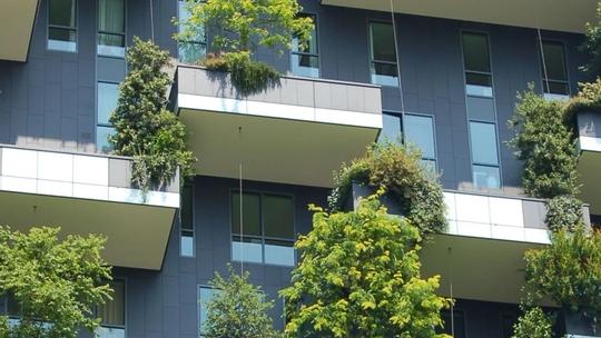 Modern building facade with balconies featuring lush greenery and trees integrated into the design.