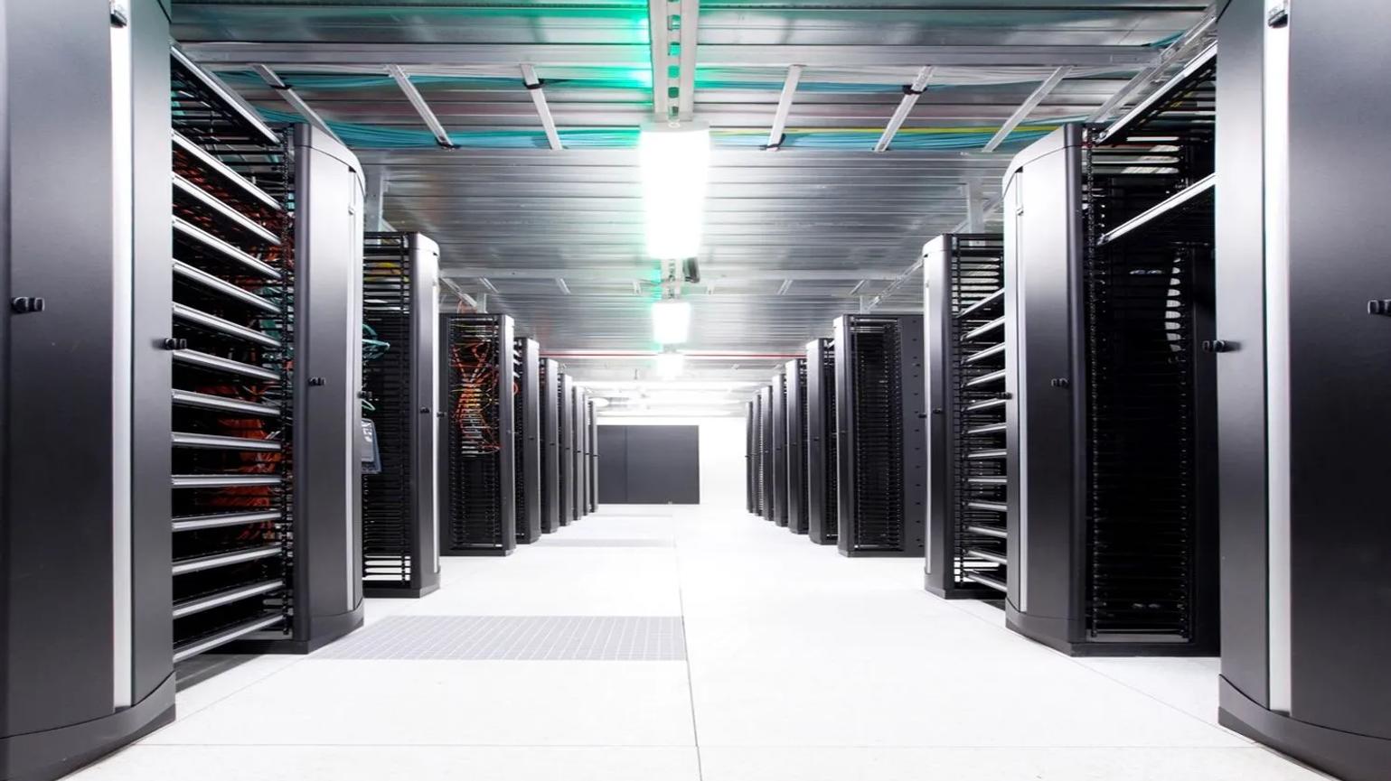 A row of server racks in a brightly lit data center with a reflective floor and overhead cable trays.