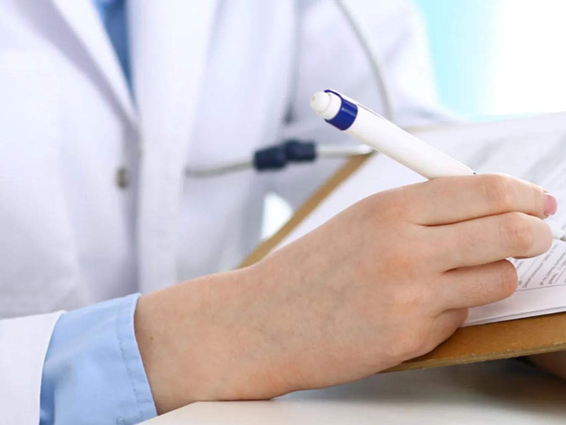 A person in a white coat writing on a clipboard with a blue and white pen.