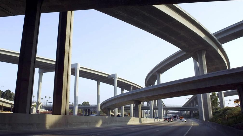 A complex network of elevated highway overpasses and ramps, with multiple levels of concrete structures intersecting against a clear sky.