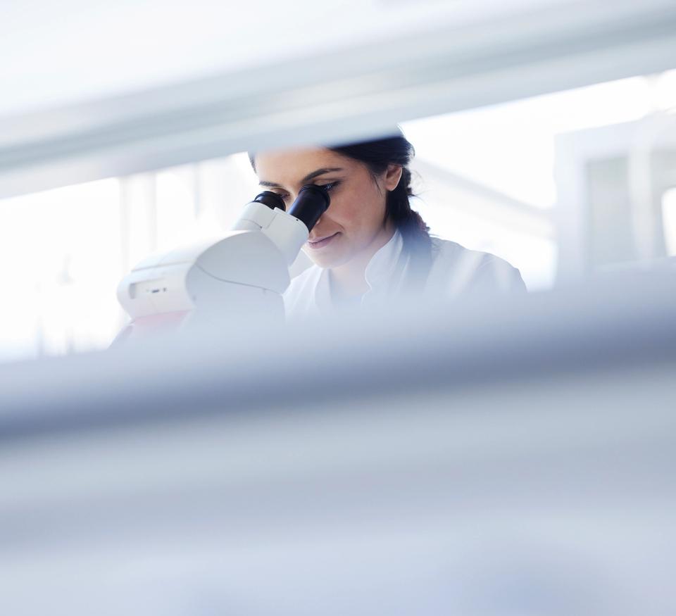 A female scientist looking into a microscope in a brightly lit laboratory.