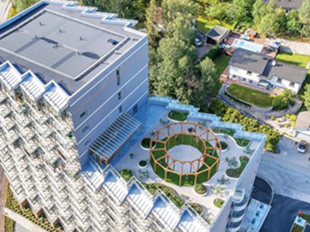 Aerial view of a modern building with a rooftop garden featuring a circular wooden structure and landscaped paths.