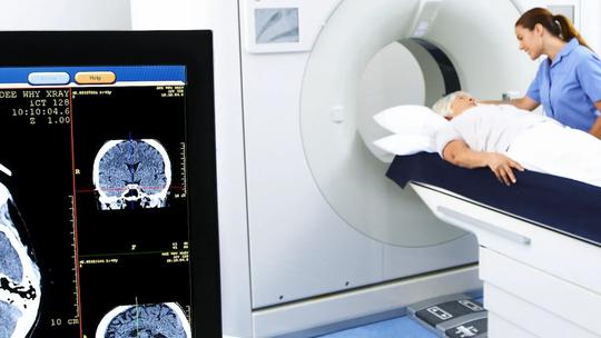 A patient lying on a CT scanner bed with a healthcare professional assisting.