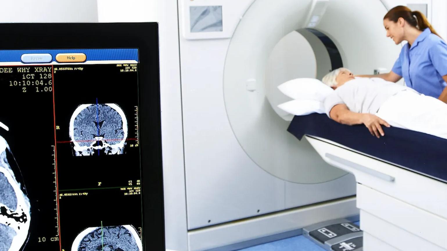 A patient lying on a CT scanner bed with a healthcare professional assisting.