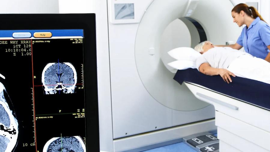 A patient lying on a CT scanner bed with a healthcare professional assisting.