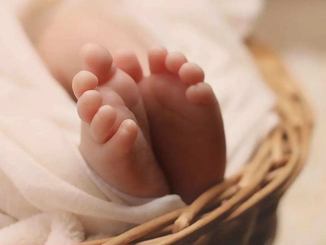 Close-up of a baby's feet resting on a soft, white blanket in a woven basket.