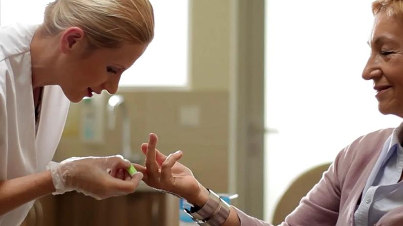 A healthcare professional is assisting a patient by performing a finger prick test in a clinical setting.