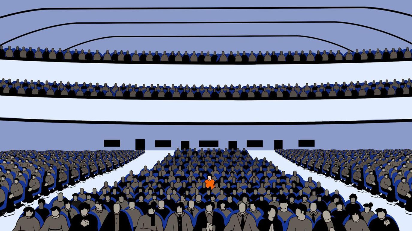 A figure in an orange shirt sits among many figures wearing dark clothes.