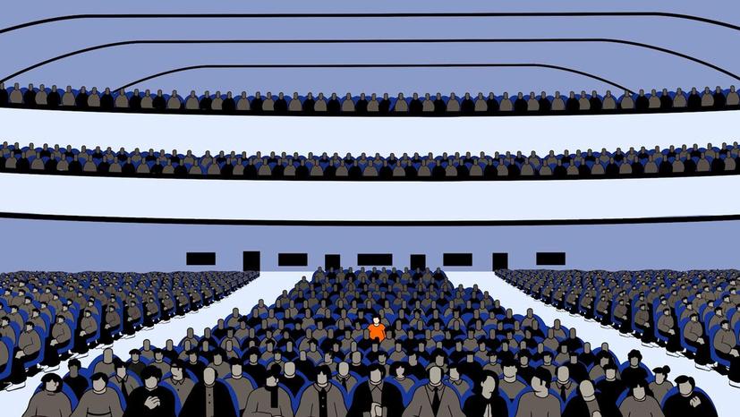 A figure in an orange shirt sits among many figures wearing dark clothes.