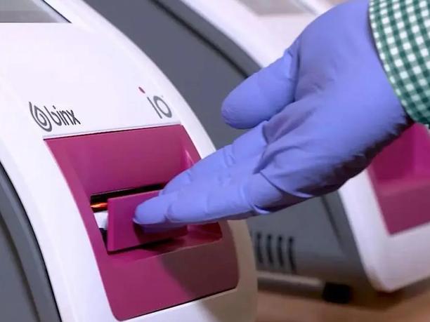 A gloved hand inserting a sample into a medical testing device labeled "binx io."