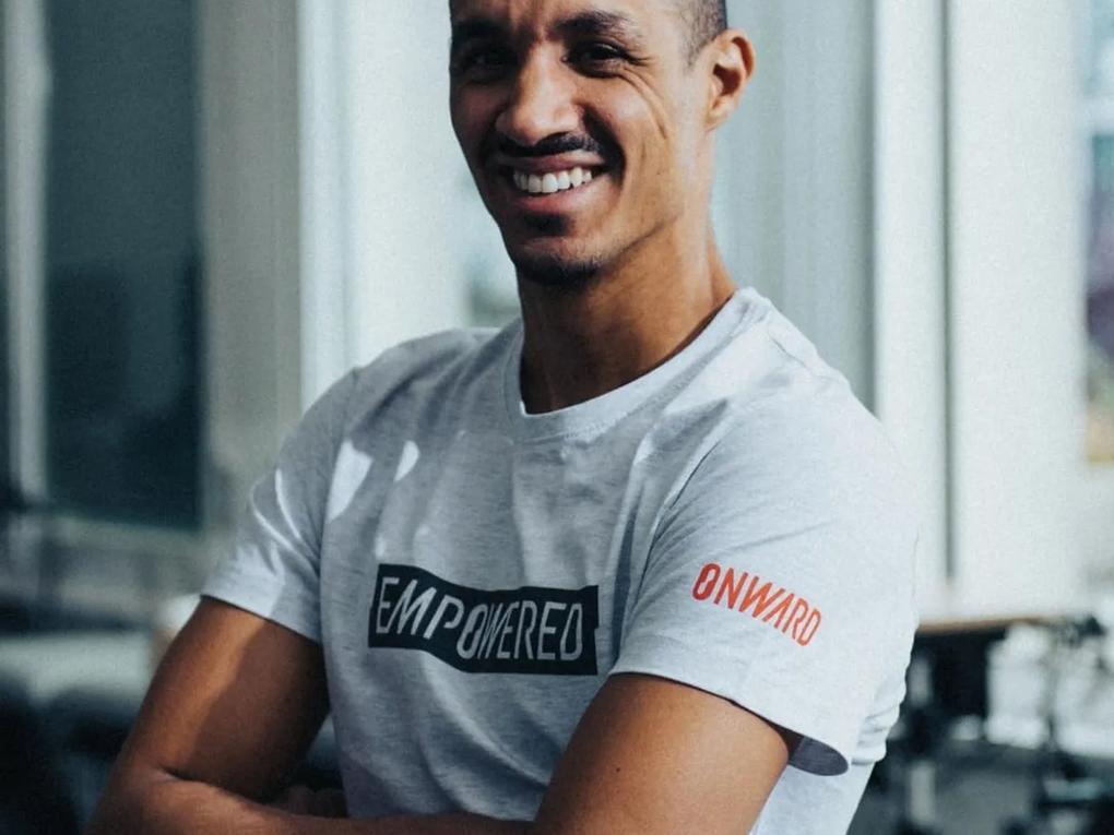 A smiling man with short hair wearing a light gray T-shirt.