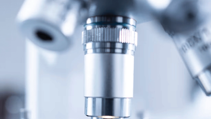 Close-up of a microscope lens focused on a slide, with a soft blue and white background.