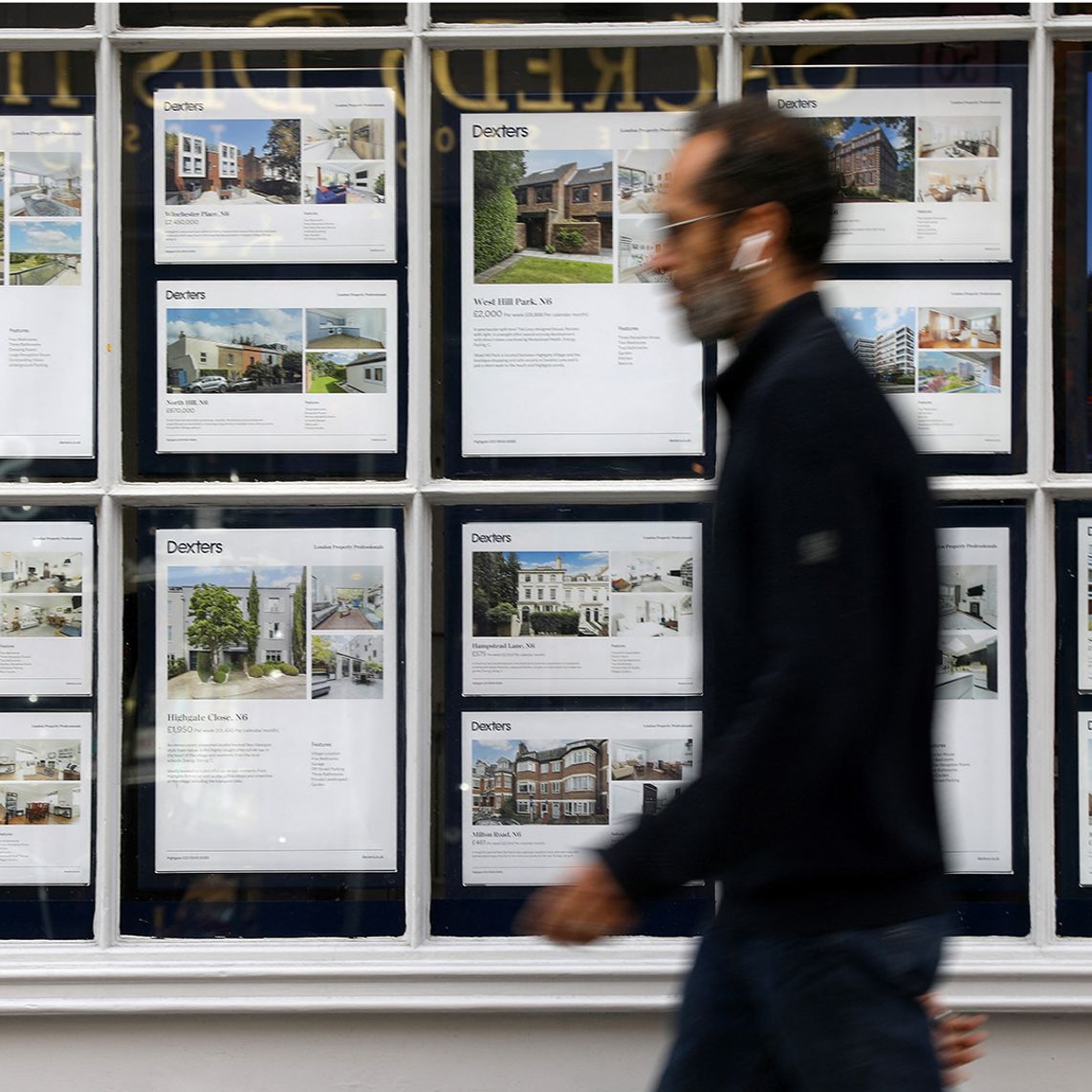 A man walks past a real estate agency window displaying property listings and photos.