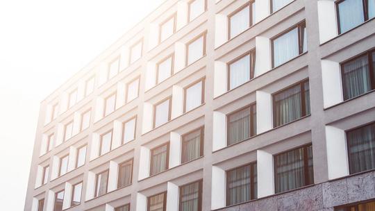 A modern building facade with a grid of windows, reflecting sunlight, creating a warm and bright atmosphere.