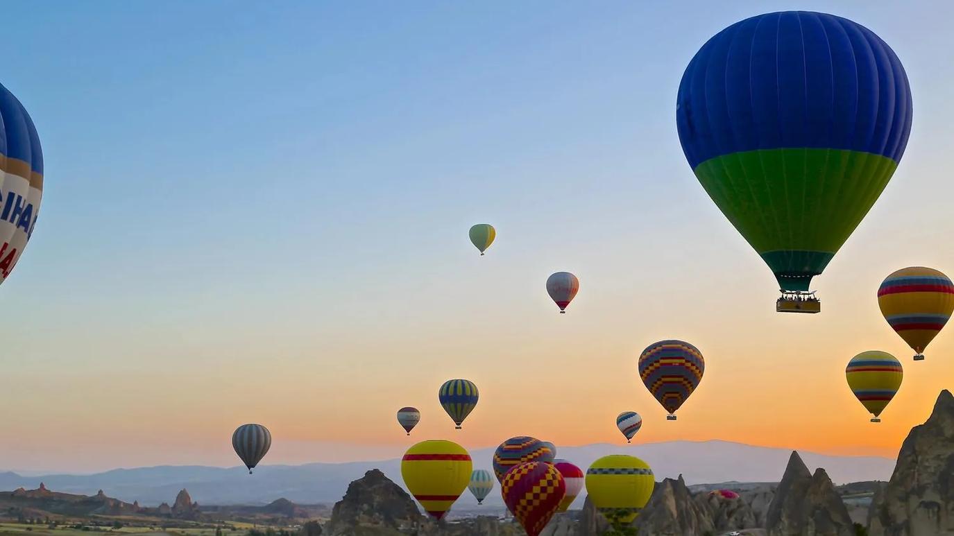 Hot air balloons of various colors floating over a rocky landscape at sunrise.
