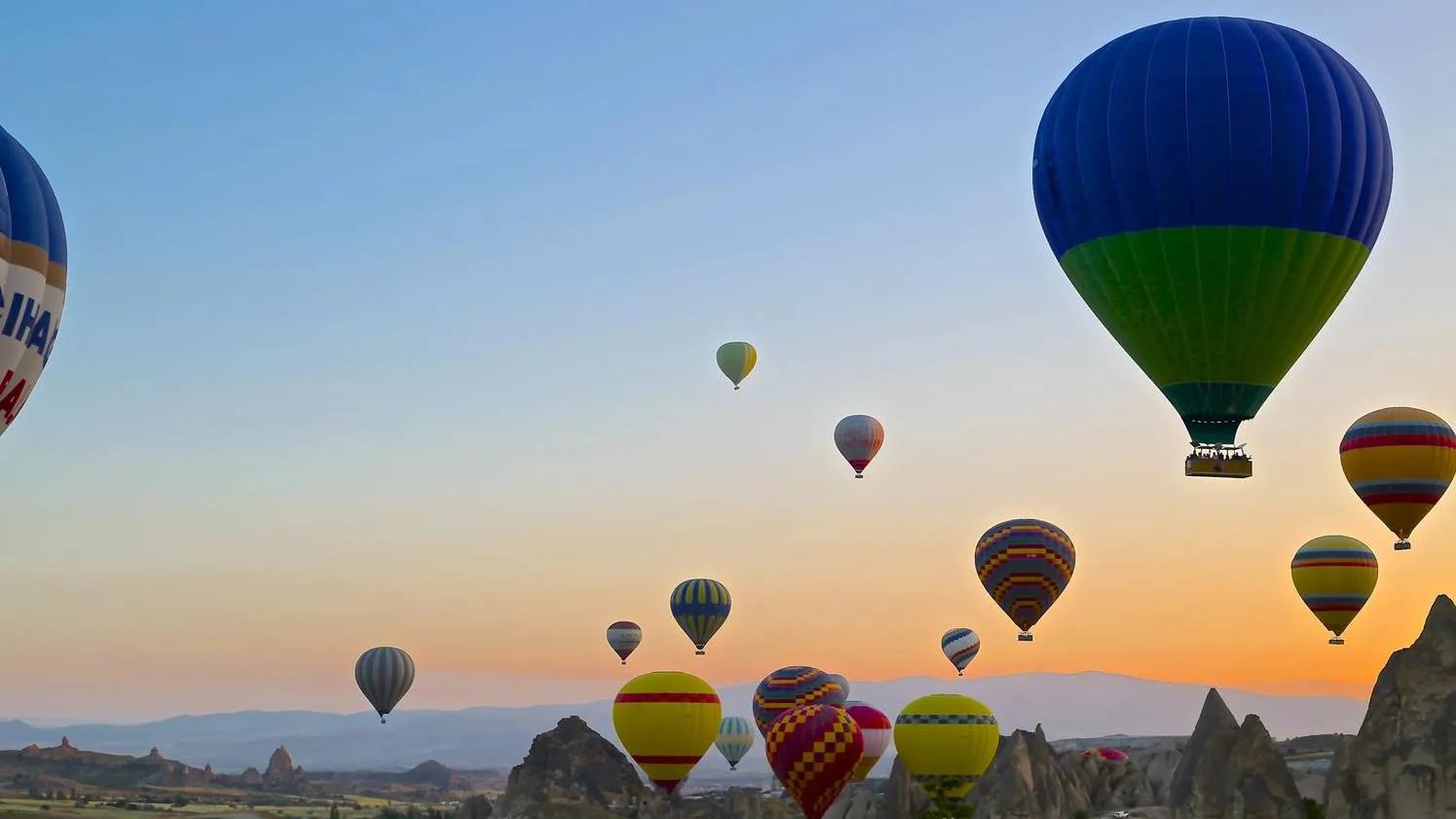 Hot air balloons of various colors floating over a rocky landscape at sunrise.