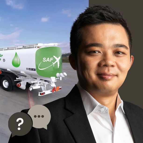 Man in a black suit with a airport and a plane in the background with a fuel tank. 