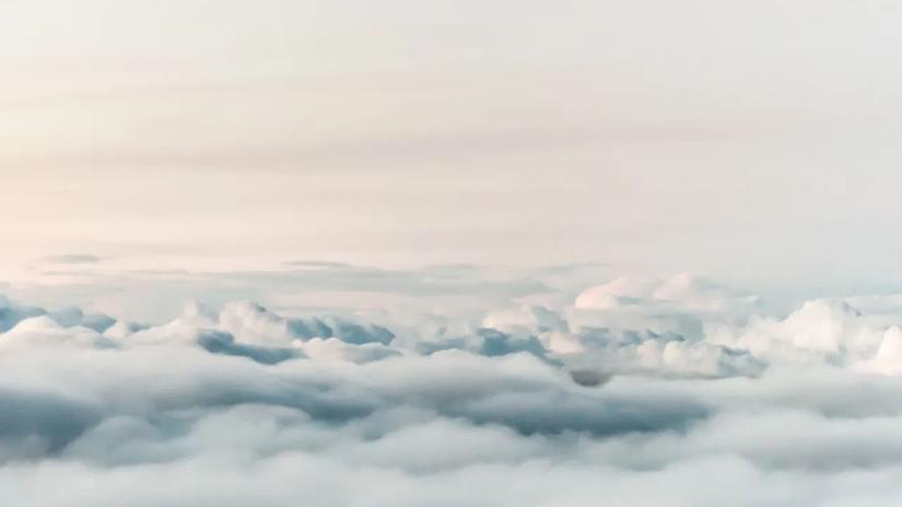 A serene view of fluffy clouds from above, with a soft, pastel sky in the background.