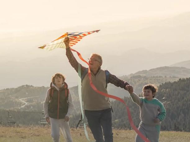 A man flying a kite with two children on a grassy hilltop.