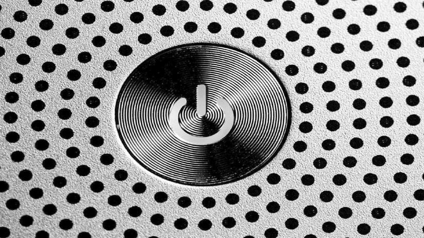 Close-up of a power button surrounded by a pattern of small black dots on a metallic surface.